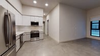 Located at 1645 Lincoln Blvd in Santa Monica, California, this single-floor unit presents a contemporary aesthetic defined by clean lines, neutral tones, and durable polished concrete flooring that runs consistently throughout the space. The open layout creates a seamless connection between the living area and kitchen, contributing to a bright, airy atmosphere enhanced by recessed lighting overhead.

The kitchen is a standout feature, outfitted with high-gloss white cabinetry extending to the ceiling for generous storage capacity. A veined stone-look backsplash adds visual interest against the white quartz countertops. Stainless steel appliances include a French door refrigerator, dishwasher, built-in microwave, and a freestanding range, providing a fully functional cooking environment.

A bedroom area features a large black-framed window overlooking an exterior balcony railing, allowing natural light to fill the room. A dedicated walk-in closet offers built-in shelving and a hanging rod for organized storage.

The bathroom includes a soaking tub with an overhead shower, brushed nickel fixtures, and an LED-backlit vanity mirror above a sleek single-sink vanity with integrated drawer storage. The consistent concrete flooring carries into this space, reinforcing the unit's cohesive modern design throughout.