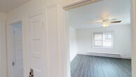 This single-floor space offers a well-maintained, move-in-ready layout with a clean, neutral aesthetic throughout. The living area features wood-look vinyl flooring, crisp white walls, a ceiling fan with light fixture, and a window overlooking the outdoors, allowing natural light to fill the room. Baseboard heating ensures year-round comfort.

The kitchen is thoughtfully designed with gray shaker-style cabinetry, warm butcher block countertops, a white subway tile backsplash, and a stainless steel sink. A stainless steel gas range and refrigerator complete the functional cooking space. A large window over the counter brings in ample natural light and adds an airy quality to the room.

The bedroom is carpeted for comfort and features two windows with horizontal blinds, baseboard heating, and bright white walls that create a calm, restful atmosphere.

The bathroom is finished in a clean, all-white palette with subway tile surrounding the bathtub and shower, wood-look flooring, a wall-mounted vanity with sink, a toilet, and a mirror. A small window provides natural ventilation.

Overall, the space presents a cohesive, updated interior with consistent flooring, modern fixtures, and a light, neutral color scheme throughout.