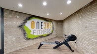 One305 Fitness at 1305 Central Ave. is a generously sized, single-floor fitness facility designed to accommodate a full spectrum of workout needs. The space is defined by a clean, modern aesthetic, featuring durable rubber flooring throughout the main exercise area, dark structural columns, and a combination of recessed and linear overhead lighting complemented by ceiling fans for air circulation.

The main workout floor is expansive and thoughtfully arranged, housing a wide variety of cardio equipment including treadmills, ellipticals, stationary bikes, and rowing machines. A dedicated selection of selectorized strength machines lines the perimeter, while stability balls and functional training accessories add versatility to the space. Large floor-to-ceiling windows along one wall flood the area with natural light and provide views of the surrounding outdoor environment, enhancing the overall atmosphere.

A separate, glass-enclosed studio is accessible through full-height glass doors and features a smooth hardwood floor, housing a row of indoor cycling bikes — ideal for spin classes or focused cardio sessions. This studio also showcases a striking branded accent wall with exposed brick and the One305 Fitness logo rendered in bold graphics.

Full-length mirrors are positioned strategically to support form checks during strength training. The facility's open layout, abundant equipment, and bright, energetic design make it a comprehensive and inviting space for fitness enthusiasts of all levels.