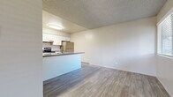 This single-floor unit offers a practical and well-appointed layout designed for comfortable everyday living. The open-concept living and dining area features light wood-style luxury vinyl flooring that extends throughout the main living spaces, creating a clean and cohesive aesthetic. Textured ceilings are present throughout, adding subtle architectural character.

The kitchen is a standout feature, equipped with white shaker-style cabinetry offering ample storage, dark granite-style countertops, and a full suite of stainless steel appliances including a refrigerator, electric range, and dishwasher. A peninsula counter separates the kitchen from the living area, providing both additional workspace and a natural division between the two spaces.

The bedrooms are generously sized, each featuring wall-to-wall carpeting in a warm neutral tone and windows fitted with horizontal blinds that allow for natural light while maintaining privacy. The rooms offer versatile layouts suitable for a variety of furniture arrangements.

The bathroom is finished with a wide vanity topped with a dark countertop, white cabinetry, a large mirror, wood-style tile flooring, and a tiled shower-tub combination. The overall design palette throughout the unit is neutral and modern, creating a bright and move-in-ready environment.