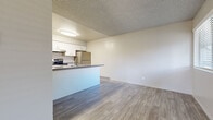 This single-floor unit offers a practical and well-appointed layout designed for comfortable everyday living. The open-concept living and dining area features light wood-style luxury vinyl flooring that extends throughout the main living spaces, creating a clean and cohesive aesthetic. Textured ceilings are present throughout, adding subtle architectural character.

The kitchen is a standout feature, equipped with white shaker-style cabinetry offering ample storage, dark granite-style countertops, and a full suite of stainless steel appliances including a refrigerator, electric range, and dishwasher. A peninsula counter separates the kitchen from the living area, providing both additional workspace and a natural division between the two spaces.

The bedrooms are generously sized, each featuring wall-to-wall carpeting in a warm neutral tone and windows fitted with horizontal blinds that allow for natural light while maintaining privacy. The rooms offer versatile layouts suitable for a variety of furniture arrangements.

The bathroom is finished with a wide vanity topped with a dark countertop, white cabinetry, a large mirror, wood-style tile flooring, and a tiled shower-tub combination. The overall design palette throughout the unit is neutral and modern, creating a bright and move-in-ready environment.