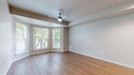 This efficient single-floor unit offers a thoughtfully arranged layout that maximizes functionality within a compact footprint. The combined kitchen and living area forms the heart of the space, where warm hardwood-style flooring flows throughout, complemented by neutral taupe walls and bright white trim. The living area is highlighted by a charming bay window configuration that floods the room with natural light and offers views of surrounding greenery, paired with a ceiling fan for added comfort.

The kitchen is well-appointed with rich dark wood cabinetry, stainless steel appliances including a refrigerator, electric range, built-in microwave, and dishwasher, along with a mosaic tile backsplash that adds a stylish accent. Recessed lighting overhead keeps the kitchen bright and functional.

The hallway connects the main living space to the bathroom and features louvered closet doors, providing practical storage solutions. The bathroom is clean and simply designed, offering a full tub-shower combination with a curved curtain rod, a dark wood vanity with a light countertop, and tile flooring that ties the room together cohesively.

Overall, the space presents a modern, move-in-ready aesthetic with consistent finishes throughout, making it a practical and inviting unit.