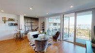 Located at 915 W Grape St in San Diego's vibrant Little Italy neighborhood, this single-floor residence blends contemporary design with bold, eclectic character. The open-concept living area is anchored by warm hardwood flooring, recessed lighting, and a striking large-scale nautical mural that serves as a dramatic focal point. Generous floor-to-ceiling sliding glass doors flood the space with natural light and open directly onto a private balcony with glass-railed views of the surrounding cityscape and palm trees beyond.

The kitchen is sleek and functional, featuring slate-toned cabinetry, a glossy subway tile backsplash, stainless steel appliances, and a compact dining area with stylish gold-accented seating. The living room offers a comfortable and curated arrangement, with a wall-mounted television and access to the balcony through expansive glazing.

The bedroom is a calm, well-appointed retreat with clean white walls, warm wood flooring, recessed lighting, and access to a built-in shelved closet area. A vibrant bathroom features bold yellow patterned wallpaper, a full tub-shower combination with white tile surround, and natural wood accents that add warmth and personality.

Overall, this residence delivers a cohesive blend of modern architecture and artistic interior design in one of San Diego's most sought-after urban neighborhoods.