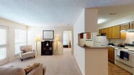 This single-story residence offers a practical and well-organized layout across several distinct living areas. The living room serves as a welcoming central space, finished with wall-to-wall carpeting, a textured ceiling, and windows fitted with blinds that allow natural light to filter through. A front entry with hardwood-style flooring transitions smoothly into the carpeted main area.

The kitchen is configured in a galley style, featuring warm wood-toned cabinetry, hardwood-style flooring, a electric range, refrigerator, and dishwasher. A pass-through opening connects the kitchen to both the living and dining areas, fostering an open, communicative flow. The dining area sits adjacent, providing a defined space for meals.

Two bedrooms offer carpeted flooring and ceiling fans, with one room currently utilized as a flexible office or study space, benefiting from a window with natural light. Both bathrooms include wood-toned vanity cabinetry, countertop sinks with large mirrors, and a full tub and shower combination with hardwood-style flooring. The overall ambiance throughout is neutral and light, with consistent warm tones creating a cohesive and comfortable living environment.
