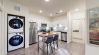 This well-appointed single-floor residence offers a thoughtfully designed layout that balances functionality and modern style throughout. The kitchen is a standout feature, showcasing white shaker cabinetry, dark granite countertops, a classic subway tile backsplash, and a full suite of stainless steel appliances including a refrigerator, range, microwave, and dishwasher. Recessed lighting and under-cabinet lights brighten the space, while light wood-look flooring adds warmth. A compact dining table with bar-height seating sits adjacent to the kitchen, creating a practical and inviting eat-in area. A dedicated in-unit stacked washer and dryer provides added convenience. The living area features vaulted ceilings, large windows with blinds that invite natural light, and direct access to an exterior door. The bedroom is carpeted for comfort, equipped with a ceiling fan, and benefits from a generous window that fills the room with natural light. The bathroom is finished with tile flooring, a granite-topped vanity with white cabinetry, a large mirror, and a shower-tub combination. Throughout the residence, neutral tones and clean finishes create a cohesive, contemporary atmosphere that is both practical and inviting.