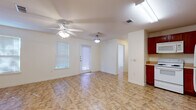 This single-floor residence offers a practical and functional layout designed for comfortable everyday living. The open living and dining area serves as the heart of the home, featuring stone-look tile flooring throughout, a ceiling fan with light fixture, and multiple windows fitted with blinds that allow for natural light control. A glass-paneled entry door provides additional brightness and connects the space to the outdoors. The kitchen is well-appointed with rich, dark-toned wood cabinetry extending to the upper walls for generous storage, light-colored countertops, a double-basin stainless steel sink, a dishwasher, and a full-size refrigerator. The layout allows for a seamless flow between the kitchen and the main living space. The bedroom is a comfortable, well-lit room featuring dual windows that offer pleasant views of surrounding greenery, a ceiling fan, and a closet with bifold doors providing ample storage. The bathroom is cleanly finished with a tiled shower-tub combination, a toilet, and a vanity with a warm wood finish. Consistent tile flooring runs throughout the unit, contributing to a cohesive and easy-to-maintain interior. Overall, the space presents a clean, neutral palette that is move-in ready and adaptable to a variety of furnishing styles.