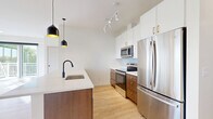 This well-appointed 2-bedroom, 2-bathroom residence in Farmington, MN offers a thoughtfully designed single-floor layout with modern finishes throughout. Light oak-toned luxury vinyl plank flooring flows seamlessly across the entire unit, complementing the crisp white walls and creating a bright, cohesive aesthetic.

The open-concept kitchen and living area serves as the heart of the home. The kitchen is outfitted with two-tone cabinetry — rich walnut lower cabinets paired with white upper cabinets featuring gold hardware — and stainless steel appliances including a refrigerator, range, and microwave. A large island with a white quartz countertop and a matte black gooseneck faucet provides additional prep space, while statement pendant lights add a contemporary touch. A herringbone tile backsplash adds subtle texture.

The primary bedroom is generously sized with multiple windows offering leafy outdoor views, flooding the room with natural light. The second bedroom is a comfortable size and includes a large sliding-door closet. Additional storage is provided by a spacious walk-in closet with built-in shelving.

Both bathrooms are finished with walnut vanity cabinets, white quartz countertops, and matte black fixtures. The primary bath features a double-sink vanity and a soaking tub. The unit also includes a private balcony, in-unit laundry, and a utility room for added convenience.
