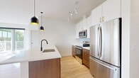 This well-appointed 2-bedroom, 2-bathroom residence in Farmington, MN offers a thoughtfully designed single-floor layout with modern finishes throughout. Light oak-toned luxury vinyl plank flooring flows seamlessly across the entire unit, complementing the crisp white walls and creating a bright, cohesive aesthetic.

The open-concept kitchen and living area serves as the heart of the home. The kitchen is outfitted with two-tone cabinetry — rich walnut lower cabinets paired with white upper cabinets featuring gold hardware — and stainless steel appliances including a refrigerator, range, and microwave. A large island with a white quartz countertop and a matte black gooseneck faucet provides additional prep space, while statement pendant lights add a contemporary touch. A herringbone tile backsplash adds subtle texture.

The primary bedroom is generously sized with multiple windows offering leafy outdoor views, flooding the room with natural light. The second bedroom is a comfortable size and includes a large sliding-door closet. Additional storage is provided by a spacious walk-in closet with built-in shelving.

Both bathrooms are finished with walnut vanity cabinets, white quartz countertops, and matte black fixtures. The primary bath features a double-sink vanity and a soaking tub. The unit also includes a private balcony, in-unit laundry, and a utility room for added convenience.