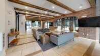 Located at 193 Jackson St in Charleston, SC, this single-floor space masterfully combines industrial, rustic, and contemporary design elements to create a dynamic and inviting environment. The interior is defined by reclaimed wood accent walls, exposed brick arches, and heavy wooden ceiling beams that lend warmth and character throughout. Soaring ceilings with exposed ductwork add an industrial edge, while large floor-to-ceiling windows along the exterior walls flood the space with abundant natural light and offer open views of the surrounding streetscape.

The main lounge areas feature multiple seating arrangements, including mid-century modern leather chairs, plush sofas, and accent chairs grouped around low tables — ideal for collaborative or social gatherings. Distinctive oversized pendant lights, including a striking black-and-yellow drum fixture, serve as bold focal points. Large-format tile and wide-plank hardwood flooring ground the various zones with texture and contrast.

A well-appointed kitchen area showcases exposed wooden ceiling beams, a generous white quartz waterfall island with bar seating, reclaimed wood cabinetry, a textured tile backsplash, and stainless steel appliances, all accented by vibrant teal pendant lighting. Additional areas provide flexible seating and open space, making this a versatile, thoughtfully designed destination in the heart of Charleston.