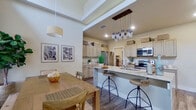 This thoughtfully designed single-story home offers a comfortable and functional layout across three bedrooms and three bathrooms. The open-concept living, dining, and kitchen area serves as the heart of the home, featuring wood-look flooring, elevated tray ceilings, and an abundance of natural light from large windows dressed with roller shades and drape panels. The kitchen is well-equipped with stainless steel appliances, granite countertops, a central island with bar seating, and ample cabinetry extending to the ceiling for generous storage. A stylish mason jar pendant light fixture adds a charming focal point above the island. The dining area comfortably accommodates a full-sized table and bench, brightened by a large window and pendant lighting. The living room is open and airy, with tray ceiling details and large windows that fill the space with natural light. The bedrooms are carpeted for comfort, each featuring ceiling fans, recessed lighting, and windows with curtains. The bathrooms are clean and functional, with one featuring built-in open shelving for linen storage. A mudroom entry connects directly to the attached garage, which includes built-in shelving and epoxy-coated flooring, providing practical additional storage. Two laundry areas add further convenience to this efficiently planned home.