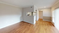 This single-story, one-bedroom, one-bathroom residence offers a thoughtfully designed layout that maximizes functionality throughout. The living area features warm hardwood-style flooring, crown molding, and a built-in bookshelf flanked by multiple windows and a sliding glass door that floods the space with natural light and provides direct outdoor access. Vertical blinds and window treatments offer privacy while maintaining the bright, open ambiance.

The kitchen is efficiently arranged with light wood cabinetry, granite-style countertops, white appliances including a range, microwave, and refrigerator, and continues the hardwood-style flooring. A pass-through window connects the kitchen to the living area, enhancing the open feel of the shared spaces.

The bedroom features plush carpeting, a ceiling fan, a window overlooking greenery, and a separate door to the outdoors. A generously sized walk-in closet with wire shelving and multiple hanging rods provides ample storage.

The full bathroom includes a granite-style vanity countertop, wood cabinetry, a tub/shower combination with white tile surround, and hardwood-style flooring, rounding out this clean, move-in-ready residence.