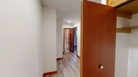 Located at 1063 Halstead Dr in Cortland, NY, this 2-bedroom, 1-bathroom unit offers a compact yet efficient single-floor layout. A central hallway with light gray wood-look flooring connects the main living areas, creating a clean and cohesive flow throughout the space. The kitchen is well-appointed with rich wood cabinetry, ample upper and lower storage, a double-basin sink, a white electric range, and a full-size refrigerator. Light hardwood-style flooring and a window with sheer curtains bring warmth and natural light into the cooking area. Both bedrooms feature soft gray carpeting and baseboard heating for year-round comfort. The spacious primary bedroom includes a large built-in closet with warm wood-toned doors and windows that allow natural light to filter in. The second bedroom offers multiple windows with curtains, providing additional brightness and ventilation. The bathroom is finished with white tile and includes a full bathtub and shower combination enclosed by a glass sliding door with chrome hardware. Throughout the unit, warm wood-toned trim and doors provide a consistent design element, complementing the neutral wall tones and creating a practical, move-in-ready living environment.
