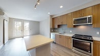 Located at 515 Lincoln Ave in San Jose, California, this modern single-floor unit offers a thoughtfully designed open-concept layout with clean lines and contemporary finishes throughout. The kitchen is a standout feature, showcasing warm wood-toned cabinetry, sleek stainless steel appliances including a range, over-the-range microwave, dishwasher, and a French door refrigerator with ice maker. Light-colored quartz countertops and a subtle tile backsplash add a refined touch, while a generous kitchen island provides additional prep and casual dining space. Recessed and track lighting illuminate the kitchen and living areas, which flow seamlessly together. Durable wood-look flooring runs throughout the main living spaces, contributing to a warm, cohesive aesthetic. A door from the living area provides access to an outdoor space, allowing natural light to fill the room. The walk-in closet offers ample storage with built-in shelving and hanging rods on multiple walls, finished with carpeted flooring. The bathroom features wood-toned cabinetry, a white quartz vanity top, a large mirror, and a combination tub and shower, all accented by the same wood-look flooring found throughout the unit. The overall ambiance is clean, modern, and functional.