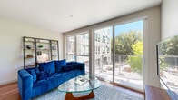 This thoughtfully designed one-bedroom, one-bathroom unit offers a functional and contemporary living experience across a single floor. The open-plan layout seamlessly connects the kitchen and living room, creating a spacious, airy feel. The kitchen is a standout feature, boasting rich wood cabinetry, stainless steel appliances including a full-size refrigerator and range, and a generous granite-topped island with bar seating and pendant lighting overhead — ideal for both cooking and casual dining. Track lighting and a mosaic tile backsplash add refined detail to the space. The living area is bathed in natural light from floor-to-ceiling sliding glass doors that open to a balcony, framing views of surrounding greenery and the urban streetscape beyond. Hardwood flooring runs consistently throughout the unit, contributing warmth and continuity. The bedroom is a comfortable retreat, featuring a ceiling fan, a large sliding-door closet, and curated wall art. The bathroom is clean and practical, finished with white tile and a full bathtub and shower combination. Overall, the unit presents a modern, cohesive aesthetic with quality finishes and a bright, inviting ambiance throughout.