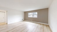 This single-story, 2-bedroom, 1-bathroom home offers a clean, modern aesthetic highlighted by light-toned wood-look flooring that runs consistently throughout every room, creating a cohesive and airy feel. The living room features neutral two-tone walls — crisp white above and warm taupe below — with a window that draws in natural light and views of the surrounding neighborhood.

The kitchen is a standout feature of the home, boasting a galley-style layout with two-tone cabinetry — white upper cabinets and dark gray lower cabinets — both accented with brushed gold hardware. White quartz countertops, a subway tile backsplash, a gold-finish sink faucet, and a full suite of stainless steel appliances, including a gas range, microwave, and dishwasher, complete this well-appointed space. A sputnik-style ceiling fixture adds a contemporary touch.

The primary bedroom is generously sized, featuring multiple windows that flood the room with natural light and offer outdoor views. The second bedroom is compact yet bright, with its own window. The bathroom is stylishly finished with a dark gray vanity, matte black fixtures, a tiled tub-shower combination, and a window for natural ventilation. The home also includes a hallway and a dedicated closet for added storage.