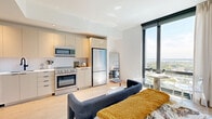 Located at 12 Church Street in New Rochelle, NY, this thoughtfully designed studio offers a seamless blend of modern finishes and efficient use of space. Light wide-plank hardwood floors run throughout, complementing the clean white walls and contemporary aesthetic.

The combined kitchen and living area serves as the heart of the studio. The kitchen is outfitted with stainless steel appliances, including a gas range, built-in microwave, and full-size refrigerator, alongside sleek light-toned cabinetry. Floor-to-ceiling windows flood the living area with natural light and frame sweeping panoramic views of the surrounding cityscape and open sky, creating an airy, open atmosphere. A compact dining area nestled by the windows takes full advantage of the scenery.

The sleeping area is well-proportioned and flows naturally from the living space, with a welcoming entry hallway that provides a sense of arrival. A slatted closet door leads to dedicated storage, while an in-unit laundry closet adds everyday convenience.

The bathroom is a standout feature, finished floor-to-ceiling in elegant marble-look tile with gold and green veining. Matte black fixtures, a floating vanity with an integrated sink, and a soaking tub complete the refined, spa-like feel. The overall ambiance of the studio is modern, bright, and polished.