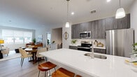 This thoughtfully designed 2-bedroom, 2-bathroom residence at 450 W Westfield Ave in Roselle Park, NJ offers a modern, open-concept layout across a single floor. The heart of the home is a sleek kitchen featuring dark wood-grain cabinetry, stainless steel appliances, a white quartz peninsula with bar seating, and a pendant-lit dining area — all flowing seamlessly into the living room. The living room is bright and welcoming, anchored by large windows that allow generous natural light and views of the surrounding neighborhood. Light wood-tone flooring runs throughout, lending a warm, cohesive feel to the space. Both bathrooms are finished with large-format tile flooring, modern dark wood-grain vanities, white quartz countertops, and clean white fixtures, with one featuring a full soaking tub. The primary bedroom offers a comfortable, well-proportioned retreat with neutral tones and ample closet space — one of five closets found throughout the residence. Additional spaces include a dedicated laundry area, pantry, utility room, and multiple hallways connecting the rooms with ease. The overall ambiance is clean, contemporary, and functional, making this a well-appointed model home in a modern residential community.