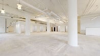 Located at 900 N Third Street in Minneapolis's North Loop neighborhood, this single-floor commercial space delivers a substantial, open-plan footprint well-suited for a variety of uses. The interior is defined by an industrial-meets-refined aesthetic, featuring exposed structural ceilings with white-painted beams, visible ductwork, and overhead pipe systems that lend the space an authentic, loft-like character.

Large multi-pane windows line the perimeter, flooding the interior with natural light and offering views of the surrounding streetscape and mature trees. A distinctive arched entry with glass doors serves as an architectural focal point, adding classical detail to an otherwise contemporary industrial framework. Sturdy structural columns are distributed throughout the open floor areas, reinforcing the building's historic character.

The layout encompasses multiple distinct zones, including expansive open areas with concrete flooring ideal for customization, as well as enclosed rooms featuring warm hardwood flooring. One area includes a full kitchenette with modern cabinetry, appliances, and a sink. Additional enclosed rooms with built-in shelving provide dedicated storage or private office potential. Glass-paneled interior doors connect zones while maintaining visual openness throughout, creating a cohesive and adaptable commercial environment.