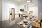 Located at 4558 Roswell Rd NE in Sandy Springs, Georgia, this single-floor residence offers a thoughtfully designed layout with modern finishes and a cohesive contemporary aesthetic throughout. The kitchen is a standout feature, showcasing crisp white cabinetry—including glass-front upper cabinets—dark granite countertops, a full suite of stainless steel appliances, and wood-look flooring. A large kitchen island with seating provides both prep space and a casual dining area, illuminated by a combination of pendant and track lighting. The living area is bright and inviting, with large windows that allow generous natural light and offer views of the surrounding exterior. A ceiling fan and track lighting provide flexible illumination, while the open layout creates a comfortable and functional gathering space. The bedroom is a serene retreat, featuring soft neutral wall tones, large windows with sheer curtains that bring in natural light, and ample room for a king-sized bed. The bathroom is finished with light tile flooring, a vanity with granite countertops, and a soaking tub with shower combination. A walk-in closet with built-in shelving and hanging rods is directly accessible from the bathroom, offering well-organized storage. This residence combines practical functionality with refined design details throughout.