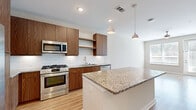 This single-floor space offers a clean, contemporary design characterized by light wood flooring and neutral warm-toned walls that flow consistently throughout. The kitchen serves as a central highlight, featuring rich walnut-toned flat-front cabinetry, granite countertop surfaces, and a full suite of stainless steel appliances including a gas range, built-in microwave, dishwasher, and French door refrigerator. A white subway tile backsplash adds a classic contrast, while a spacious center island with matching granite provides additional prep and dining space. Pendant lighting above the island enhances both function and style.

The living area is generously sized, benefiting from multiple windows and a door that invite natural light, with a ceiling fan adding comfort. The bedrooms are comfortably proportioned, each featuring ceiling fans, ample natural light from large windows, and access to a walk-in closet outfitted with wire shelving systems. The bathroom is well-finished, with a granite-topped vanity, walnut cabinetry, a tiled tub-shower combination, and recessed lighting, maintaining the cohesive modern aesthetic found throughout the space.