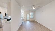 This single-floor unit offers a clean, contemporary design characterized by crisp white walls, light wood-style flooring, and an abundance of natural light. The open-concept living and dining area is spacious and airy, featuring a ceiling fan with integrated lighting, a glass-paneled entry door, and multiple windows fitted with horizontal blinds that frame views of the surrounding community. A pendant chandelier marks the dining area, which flows seamlessly into the adjoining spaces.

The kitchen is well-appointed with tall white shaker cabinetry, light granite countertops, a subtle grey subway tile backsplash, and a full suite of stainless steel appliances including a refrigerator, range, built-in microwave, and dishwasher. The layout provides ample counter and storage space.

The bedroom areas continue the consistent flooring and neutral palette, with windows offering outdoor views and generous wall space. The entry foyer is clean and functional, with direct access to additional rooms via a hallway corridor.

Throughout the unit, the design is cohesive and modern — light tones, clean lines, and thoughtful lighting create a bright, welcoming ambiance that feels both practical and refined.