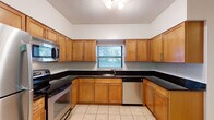 This two-floor residence offers a thoughtfully designed layout with functional and comfortable living spaces throughout. The kitchen is a standout feature, boasting warm honey-toned cabinetry, dark granite countertops, and a full suite of stainless steel appliances including a range, microwave, dishwasher, and refrigerator. Light tile flooring and a window above the sink bring in natural light, while an adjacent laundry area adds everyday convenience. The living room is expansive and inviting, anchored by a classic fireplace with a white mantel and framed by built-in shelving and cabinetry on either side — ideal for display or storage. Plush wall-to-wall carpeting, crown molding, and a textured ceiling complete the refined look of the main living area. The bedrooms are generously sized, each featuring soft carpeting and ceiling fans for year-round comfort. One bedroom includes sliding glass doors that open to a private balcony with exterior views. The bathrooms are clean and functional, with one offering a full tub-shower combination and tile flooring, and another presenting a windowed half-bath layout. The staircase connects both floors with an elegant banister, contributing to the home's cohesive and classic design aesthetic throughout.