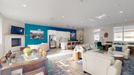 Located at 38 Westgate Dr. in Dover, NH, this single-floor community space offers a welcoming, open-concept layout that seamlessly integrates a fully equipped kitchen with a spacious living and lounge area. The design is anchored by striking teal accent walls that provide bold contrast against crisp white walls, light gray wood-look flooring, and a clean white ceiling with recessed lighting throughout.

The kitchen features white shaker cabinetry, a classic subway tile backsplash, and an expansive quartz countertop island with dramatic veining — ideal for gathering and casual dining. Bar-height seating lines the island, complemented by a stainless steel refrigerator and a matte black undermount sink. Pendant lighting above the island adds a refined finishing touch.

The living area is generously proportioned, accommodating multiple seating arrangements including plush cream leather sofas and armchairs arranged around area rugs and wood accent tables. A wall-mounted flat-screen TV serves as a focal point, while a dining table with wood chairs provides additional gathering space. Large windows along the perimeter invite abundant natural light and views of the surrounding community. The overall ambiance is modern, inviting, and thoughtfully designed for both relaxation and social interaction.