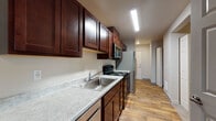 Located at 352 North Beck Road in Post Falls, Idaho, this single-floor unit offers a well-organized layout designed for comfortable everyday living. The entry opens into a hallway finished with durable wood-look flooring that extends throughout the main traffic areas, providing a warm and cohesive aesthetic. A utility panel and wall-mounted heating unit are conveniently accessible along the corridor.

The galley-style kitchen is a standout feature, outfitted with rich dark-stained wood cabinetry offering generous storage both above and below the counters. Light-toned countertops provide a pleasant contrast, and the space is equipped with a stainless steel sink, an electric range, and an over-the-range microwave, making it fully functional for daily meal preparation.

The living area is carpeted in a neutral tone and receives natural light through a large window fitted with vertical blinds. A glass-paneled exterior door leads outside, further brightening the space and offering convenient access. The room provides ample open space suitable for a variety of furniture arrangements.

The bathroom features wood-look flooring consistent with the rest of the unit, a wide vanity with a marble-style countertop and large mirror, and a high-set window that allows natural light while maintaining privacy. The overall design is clean and neutral throughout, offering a move-in ready environment.