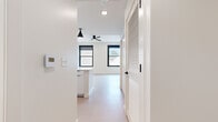 Located at 1303 Baltimore Ave in the heart of downtown Kansas City, Missouri, this thoughtfully designed single-floor unit offers a clean, contemporary aesthetic throughout. The open living area is bathed in natural light streaming through black-framed windows that frame urban views of the surrounding cityscape, creating a bright and airy atmosphere. Light-toned flooring runs throughout the main living space, complementing the crisp white walls and recessed lighting overhead. A ceiling fan adds both function and a modern touch to the living area.

The kitchen is a standout feature, centered around a generous white quartz-topped island with an undermount sink — ideal for both meal preparation and casual dining. White cabinetry extends to the ceiling, maximizing storage, while stainless steel appliances, including a refrigerator, microwave, and range, deliver a polished, functional finish. A sleek pendant light anchors the kitchen space with style.

The hallway connects the living areas to the bathroom and includes a louvered storage closet. The bathroom is finished with large-format white tile flooring, a warm wood-toned vanity with a white quartz countertop, an undermount sink, and a large mirror, all accented with black hardware for a contemporary look. The overall ambiance is modern, minimal, and move-in ready.