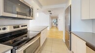 Located on Rue Drummond in the heart of downtown Montréal, this well-appointed 2-bedroom, 2-bathroom residence offers a clean, modern aesthetic across a single thoughtfully designed floor. The open living room is a standout feature, showcasing warm light hardwood flooring, crisp white walls, and a wall of floor-to-ceiling sliding glass doors that open onto a private balcony with sweeping city views. The balcony provides an inviting outdoor retreat with direct sightlines to Montréal's vibrant urban skyline. The kitchen is efficiently designed with white cabinetry, grey countertops, tile flooring, stainless steel appliances, and a window that brings in natural light. A long corridor connects the main living areas to the two generously sized bedrooms, each featuring the same warm hardwood floors and windows with neighbourhood views, creating bright and restful retreats. The spacious primary bedroom offers ample room for furnishing. The two bathrooms are finished in a contemporary style — one features neutral tile walls, a white vanity with drawers, and recessed lighting, while the second is a clean, minimalist powder room. Track lighting in the living area adds a modern touch, and in-unit laundry is visible along the hallway, adding convenience to this polished urban residence.