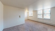 Located in Detroit, MI 48202, this studio offers a well-organized single-floor layout designed for practical, comfortable living. The main living area is generously proportioned relative to its footprint, featuring neutral-toned carpet flooring, clean white walls, and multiple windows that invite natural light and provide views of the surrounding urban streetscape. A baseboard heating system runs along the exterior wall, ensuring year-round comfort. An intercom unit is conveniently mounted near the entrance.

The open-concept layout flows seamlessly into a compact kitchen equipped with a white electric range, refrigerator, and warm wood-toned cabinetry — providing all the essentials in an efficient arrangement. A hallway connects the main space to the bathroom and entry door, contributing to a sense of defined zones within the open floor plan.

The full bathroom features tile flooring in a neutral stone-like finish, a wood-vanity with an integrated sink, a standard toilet, and a tub-shower combination with a window above for natural ventilation. Warm wood-toned doors are featured throughout, adding a classic residential feel.

A closet accessible from the main living area provides dedicated storage. The entry door features a keyed lock for security. Overall, the space presents a clean, functional layout well-suited for single occupancy in an urban setting.