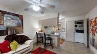 This efficient one-bedroom, one-bathroom residence is thoughtfully designed to maximize every square foot of its single-floor layout. The open-concept living area serves as the heart of the home, featuring soft carpet flooring, a ceiling fan with light fixture, and a textured ceiling. A comfortable seating arrangement anchors the space, complemented by a bold area rug and decorative wall art that add personality and warmth. A window with blinds allows natural light to filter in, brightening the room.

The kitchen flows directly from the living area and is defined by a raised breakfast bar with seating for two, making it ideal for casual dining. The kitchen is equipped with standard appliances including a refrigerator, microwave, and range, all set against light cabinetry and tile flooring that transitions seamlessly from the cooking space.

The bedroom is a peaceful retreat featuring plush carpet, a ceiling fan, and two windows dressed with blinds that invite natural light while maintaining privacy. The room comfortably accommodates a full-sized bed and additional furniture such as a dresser, offering practical storage.

The bathroom is clean and functional, featuring tile flooring, a shower-tub combination with sliding glass doors, a toilet, and overhead cabinetry for storage. Overall, the space presents a cozy, practical layout suited for efficient everyday living.