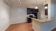 Located at 3210 Open Field Ln in Charlotte, NC, this single-floor residence offers a well-designed layout with a cohesive blend of functional and comfortable living spaces. The kitchen is a standout feature, showcasing rich dark cabinetry, granite countertops, and stainless steel appliances including a refrigerator, range, and over-the-range microwave. A peninsula with a pendant light and track lighting above adds a modern touch, while light hardwood-style flooring and crown molding enhance the overall finish. The galley-style kitchen corridor provides ample upper and lower cabinet storage alongside a stainless steel sink. The living area flows naturally from the kitchen, offering an open and airy feel. The bedrooms feature neutral carpet flooring and windows fitted with blinds that allow for natural light. One bedroom includes a walk-in closet with a built-in shelving and rod system, providing generous storage. The bathroom is finished with light hardwood-style flooring, a white tiled tub-shower combination with chrome fixtures, a toilet, and a vanity with dark cabinetry and a white countertop. Throughout the home, neutral wall tones and clean finishes create a bright, move-in-ready atmosphere.