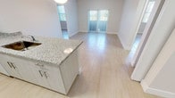 Located at 14981 SW 283 St in Homestead, FL, this single-story unit offers a clean, modern layout designed for comfortable living. The open-concept kitchen serves as the centerpiece of the main living area, featuring a peninsula with granite countertop and an integrated sink, light gray cabinetry, white appliances including a refrigerator, electric range, and microwave, and a walk-in pantry closet. A pendant light fixture above the peninsula adds a refined touch to the space.

The kitchen flows seamlessly into the living and dining areas, which are bathed in natural light from sliding glass doors fitted with vertical blinds. Light-toned large-format tile flooring extends throughout, creating a cohesive and airy feel. The living area provides direct outdoor access, enhancing the connection to natural light and ventilation.

The bedrooms are well-proportioned, each with the same light tile flooring and ample wall space. The electrical panel is conveniently integrated near the entry. The bathrooms are finished with granite-topped vanities, white cabinetry, large mirrors, and tub-shower combinations with tile surrounds. Clean white walls and recessed lighting throughout contribute to a bright, neutral palette that defines this well-appointed Homestead residence.