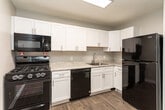 Located on W Friendly Avenue in Greensboro, North Carolina, this single-floor unit offers a clean, modern aesthetic with consistent wood-look flooring carried throughout every room. The open living area is bright and welcoming, with large windows dressed in blinds that invite natural light and provide views of the surrounding neighborhood. Neutral gray walls complement the warm flooring tones, creating a cohesive and versatile interior palette.

The kitchen is a standout feature, outfitted with crisp white shaker-style cabinetry, brushed nickel hardware, and light granite-style countertops. Black appliances — including a gas range, over-the-range microwave, dishwasher, and refrigerator — provide a bold contrast against the white cabinetry. A stainless steel sink with a modern faucet completes the functional workspace.

The bedroom is generously sized, featuring the same neutral tones and wood-look flooring, with a window that brings in natural light. A walk-in closet with dual shelving on opposing walls offers ample storage. The bathroom is finished in a clean, all-white scheme with a vanity featuring a medicine cabinet mirror, a full tub-shower combo with a curved rod, and wood-look tile flooring that ties the space together seamlessly.