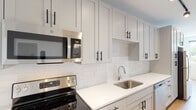 Located at 1116 Missouri Ave in St. Louis, Missouri, Unit 507 presents a thoughtfully designed single-floor residence that blends contemporary finishes with a clean, functional layout. The kitchen is a standout feature, showcasing white shaker-style cabinetry extending floor to ceiling, accented by matte black hardware that adds a modern contrast. Crisp white quartz countertops and a white subway tile backsplash complement the full suite of stainless steel appliances, including an electric range, built-in microwave, dishwasher, and refrigerator. Track lighting overhead provides focused illumination throughout the space. Warm-toned wood-look flooring flows consistently through the living areas, creating a cohesive and inviting atmosphere. The bedroom is a well-proportioned, light-filled space equipped with a ceiling fan and recessed lighting. The bathroom continues the unit's refined aesthetic with a white vanity topped with quartz, a large mirror, and matte black fixtures that tie the design together. Throughout the unit, crisp white walls and recessed lighting contribute to a bright, airy ambiance, making the space feel open and well-appointed.