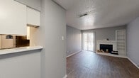 This single-floor, 2-bedroom, 2-bathroom unit offers a practical and well-organized layout designed for comfortable living. The open living room is a standout feature, showcasing rich hardwood-style flooring, a classic fireplace with a white brick surround, and built-in shelving. A sliding glass door floods the space with natural light and provides access to the outdoors, while a textured ceiling adds a distinctive architectural element throughout.

The kitchen is efficiently designed with crisp white cabinetry, light stone-look countertops, and black appliances, including a full-size refrigerator and dishwasher. A pass-through counter connects the kitchen to the living area, enhancing the sense of openness.

A long hallway leads to the two bedrooms, each carpeted for warmth and comfort and equipped with ceiling fans. The primary bedroom offers a generous layout with ample wall space, while the secondary bedroom features a window with outdoor views. Both bathrooms are clean and functional, each offering a full tub-shower combination with white tile surrounds.

Consistent grey-toned walls, white trim, and wood-look flooring in the main areas create a cohesive, neutral aesthetic throughout the unit, making it move-in ready and easy to personalize.