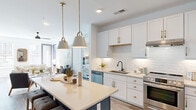Located at 1000 Lakeside Terrace Ct in Wake Forest, NC, this well-appointed residence offers three bedrooms and five bathrooms across a single floor. The open-concept kitchen is a standout feature, showcasing crisp white shaker cabinetry with gold hardware, a subway tile backsplash, stainless steel appliances including a gas range and dishwasher, a deep undermount sink with a matte black faucet, and a spacious island with pendant lighting—ideal for both cooking and entertaining. Wood-look flooring flows throughout, adding warmth and continuity to the space. The living room is bright and welcoming, with large windows and a glass door that invite natural light and provide outdoor views of the surrounding neighborhood. A ceiling fan adds comfort to the airy layout. The bedrooms are comfortably sized, with the primary bedroom offering a tranquil retreat. The bathrooms are cleanly designed, featuring large-format white tile in the showers with matte black fixtures, and wood-tone flooring with white vanities accented by gold hardware in the full baths. Accessibility-friendly grab bars are present in select bathrooms. A dedicated laundry closet with full-size washer and dryer and overhead shelving rounds out this thoughtfully designed home.