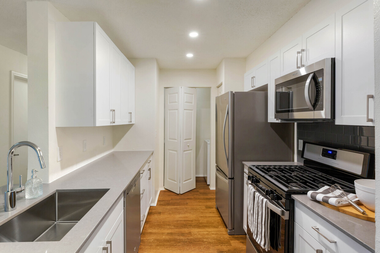 Paquete renovado I cocina con gabinetes blancos, encimeras de cuarzo gris, salpicadero de azulejos de vidrio y electrodomésticos de acero inoxidable, y pisos de madera de superficie dura - Avalon at Lexington