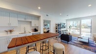 Located at 20060 Prairie St in the Chatsworth neighborhood of Los Angeles, this modern single-story residence showcases a clean, contemporary design with warm hardwood flooring flowing consistently throughout. The open-concept layout seamlessly connects the kitchen, dining area, and living room, creating a bright and cohesive living environment. Recessed lighting and crisp white walls amplify the sense of openness throughout the home.

The well-appointed kitchen features light shiplap-style cabinetry, stainless steel appliances including a French door refrigerator, microwave, and range, complemented by white quartz countertops and a subway tile backsplash. A wood-top kitchen island with bar stools serves as both a functional workspace and casual dining spot.

The living area is anchored by large sliding glass doors that open onto a private outdoor terrace, offering views of palm trees and native cacti — a distinctive Southern California backdrop. The bedroom offers a calm, sunlit retreat with recessed lighting and a window providing natural light.

The bathroom is finished with a floating vanity, backlit mirror, hexagonal floor tile, and warm gold-toned hardware accents, delivering a polished, spa-like aesthetic. Overall, this residence combines modern functionality with inviting, thoughtfully curated design details throughout.