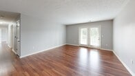 Located at 7121 Fern Ridge Rd in Louisville, Kentucky, this single-story, 3-bedroom, 2-bathroom home offers a functional and well-organized layout with consistent warm-toned hardwood-style flooring throughout. The open living area is highlighted by a textured ceiling, a ceiling fan, and French doors that invite natural light and provide outdoor views. The kitchen is outfitted with white shaker-style cabinetry, light granite-look countertops, and black appliances including a refrigerator, range, built-in microwave, and dishwasher, all set atop matching hardwood-style flooring. The spacious primary bedroom features ample room for furnishings, while the two additional bedrooms each include windows that bring in natural light and offer exterior views. The two bathrooms are finished with white vanity cabinetry, white countertops, and hardwood-style flooring; one features a large vanity with overhead lighting, while the other includes a full shower-tub combo. A dedicated laundry room provides washer and dryer hookups along with overhead wire shelving for additional storage. A hallway and closet round out the home's practical layout, making this a well-appointed and move-in-ready residence.