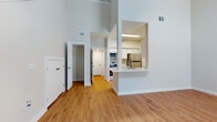 This two-story residence is defined by its impressive architectural design, most notably the dramatic soaring ceilings in the main living area that create an expansive, open atmosphere. Warm hardwood-style flooring runs consistently throughout the home, lending a cohesive and inviting character to every room.

The main living area is generously proportioned, connecting seamlessly to a dedicated dining space that features an elegant arched interior window and an exterior window with blinds, drawing in ample natural light. A staircase with a clean white railing leads to the second floor, accompanied by a double-door closet at its base for convenient storage.

The kitchen is efficiently laid out and accessible via a pass-through opening with a countertop bar that overlooks the living and dining areas. It is equipped with stainless steel appliances including a refrigerator, electric range, and over-the-range microwave, complemented by crisp white cabinetry, light countertops, and a sink. A pantry or utility closet with a bifold door provides additional storage directly within the kitchen.

The bedrooms are well-sized, each featuring ceiling fans and hardwood-style flooring. Several rooms benefit from windows that invite natural light and outdoor views. The entryway is welcoming, with a front door framed by a sidelight window and direct access to the main living spaces. Overall, the home presents a clean, neutral palette with functional, well-connected layouts across both floors.