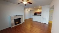 This single-floor residence offers a well-organized, open layout that connects the living area, kitchen, and utility spaces cohesively. The living room serves as the central gathering space, highlighted by a tile-surround electric fireplace that adds warmth and visual interest to the room. Two ceiling fans with integrated lighting are positioned throughout the living area, promoting air circulation and providing ambient illumination alongside recessed lighting. Hardwood-style flooring runs consistently throughout the main living spaces, lending a clean and unified appearance.

The kitchen is designed for functionality, featuring rich, dark wood cabinetry that extends to the ceiling for ample storage. Dark granite-style countertops complement the cabinetry, while black appliances — including a refrigerator, range, and built-in microwave — provide a cohesive aesthetic. A raised breakfast bar with seating overhang connects the kitchen to the living area, making it ideal for casual dining or entertaining.

A dedicated laundry area is accessible from the main living space, housing a washer and dryer unit. The bathroom includes a combination tub and shower, a toilet, and a dark wood vanity with a granite-style countertop, finished with tile-style flooring for easy maintenance.