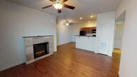 This single-floor residence offers a well-organized, open layout that connects the living area, kitchen, and utility spaces cohesively. The living room serves as the central gathering space, highlighted by a tile-surround electric fireplace that adds warmth and visual interest to the room. Two ceiling fans with integrated lighting are positioned throughout the living area, promoting air circulation and providing ambient illumination alongside recessed lighting. Hardwood-style flooring runs consistently throughout the main living spaces, lending a clean and unified appearance.

The kitchen is designed for functionality, featuring rich, dark wood cabinetry that extends to the ceiling for ample storage. Dark granite-style countertops complement the cabinetry, while black appliances — including a refrigerator, range, and built-in microwave — provide a cohesive aesthetic. A raised breakfast bar with seating overhang connects the kitchen to the living area, making it ideal for casual dining or entertaining.

A dedicated laundry area is accessible from the main living space, housing a washer and dryer unit. The bathroom includes a combination tub and shower, a toilet, and a dark wood vanity with a granite-style countertop, finished with tile-style flooring for easy maintenance.