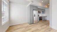 Located in Salt Lake City, UT, this modern studio offers a thoughtfully designed, single-level layout that maximizes every square foot. The open-concept living area is bathed in natural light through large windows with horizontal blinds, complemented by crisp white walls and light wood-tone luxury vinyl flooring that runs throughout the entire unit, creating a cohesive and airy feel.

The kitchen is seamlessly integrated into the living space and features sleek gray flat-front cabinetry, stainless steel appliances including a French door refrigerator, electric range, and over-the-range microwave, as well as a white countertop with an undermount sink. A pass-through window connects the kitchen area to the bedroom space, enhancing the open flow of the layout.

The bedroom area is a clean, minimalist space with ample room for furnishings, recessed lighting, and a continued neutral palette that promotes a calm atmosphere. A hallway connects the main living areas to the full bathroom, which includes a wide dark gray vanity with a white countertop, a framed mirror, globe pendant lighting, wood-look tile flooring, and a bathtub with shower. The overall design reflects a clean, contemporary aesthetic well-suited for modern urban living.