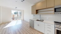 Located at 4770 Telegraph Ave in Oakland, CA, this single-floor unit offers a thoughtfully designed interior with a clean, contemporary aesthetic throughout. The open-concept layout connects the kitchen and living area seamlessly, creating a functional and inviting space bathed in natural light.

The kitchen is outfitted with modern stainless steel appliances, including a full range with oven, over-the-range microwave, dishwasher, and a deep single-basin sink fitted with a flexible spray faucet. Cabinetry features a two-tone design — crisp white lower cabinets with brushed hardware and warm wood-toned upper cabinets — complemented by an eye-catching hexagonal tile backsplash and light quartz countertops. Light wood-look flooring extends throughout the main living areas, adding warmth to the neutral white walls.

The living area benefits from large sliding glass doors that open to a private balcony, offering outdoor views and generous natural light. A separate bedroom includes a sliding-door closet and continues the same light flooring palette. The unit includes multiple bathrooms: one features a frameless glass walk-in shower with large-format tile surround, while another offers a more accessible layout with grab bars and tile flooring. The overall ambiance is bright, clean, and move-in ready.