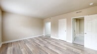 This Presidential Greens A1D unit offers 500 square feet of thoughtfully arranged living space across a single floor, comprising two bedrooms, one bathroom, a kitchen, and a hallway. The living area features light-toned luxury vinyl plank flooring and warm neutral-painted walls, with multiple windows allowing natural light and outdoor views of the surrounding community. A dedicated entry door with transom window opens directly into this space. The kitchen is efficiently designed with white cabinetry, a subway tile backsplash, stainless steel appliances including a range and refrigerator, and LVP flooring, with a window overlooking greenery. The primary bedroom measures 220 square feet and is finished with plush neutral carpet and a built-in overhead shelf, providing functional storage. The second bedroom also features carpet flooring and clean, neutral walls. The bathroom is finished in a bright, all-white palette with subway tile wainscoting, LVP wood-look flooring, a white vanity with brushed nickel hardware, and a toilet, creating a clean and modern aesthetic. White trim and baseboards are consistent throughout, lending a cohesive, well-maintained feel to the entire unit.