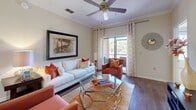 Located at 10011 Balaye Run Dr in Tampa, FL, this single-story 2-bedroom, 3-bathroom home offers a well-designed layout across a comfortable footprint. The open-concept living and dining area features rich hardwood-style flooring, crown molding, and ceiling fans, creating a polished yet inviting atmosphere. A large sliding glass door floods the living room with natural light and provides views of the surrounding greenery. The adjacent dining area is accented by an elegant chandelier and connects seamlessly to the kitchen. The kitchen is equipped with granite countertops, light wood cabinetry, a breakfast bar peninsula, and tile flooring, offering both style and functionality. The primary bedroom is a spacious retreat with plush carpeting, a ceiling fan, and a bold accent wall, complemented by an en-suite bathroom featuring an extended granite vanity and tile flooring. The second bedroom is equally comfortable, also with carpeting and a ceiling fan. The bathrooms throughout echo the home's consistent design language, showcasing granite countertops, white cabinetry, and tub-shower combinations. Additional conveniences include a dedicated laundry area, hallway with closet storage, and crown molding details throughout that lend the home a refined character.