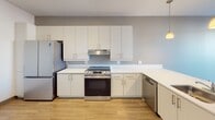 Located at 401 Justison Street in Wilmington, Delaware, this single-floor residence offers a clean, modern aesthetic throughout. The open-concept kitchen is well-equipped with stainless steel appliances, including a French door refrigerator, electric range, and dishwasher, all complemented by white flat-panel cabinetry, white quartz countertops, and warm hardwood-style flooring. Pendant lighting fixtures hang above the kitchen peninsula, adding a contemporary touch, while a window at the end of the space draws in natural light. The living area flows seamlessly from the kitchen, offering an open and versatile layout. A bedroom features a large window with views of the surrounding neighborhood and a stylish sliding barn door, adding a modern architectural detail. The spacious hallway connects multiple rooms and closets, providing generous storage options throughout. The bathroom is designed with accessibility in mind, showcasing a full soaking tub and shower combination with classic white subway tile surround, chrome grab bars, and hardwood-style flooring. Throughout the unit, light-toned luxury vinyl plank flooring, crisp white walls, and consistent modern finishes create a cohesive and inviting living environment.