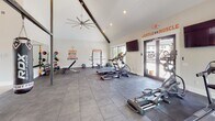 Located on Pointe Grand Drive in Augusta, Georgia, this single-floor fitness center is designed to deliver a comprehensive workout experience. The space features striking vaulted ceilings with exposed dark wood beams, an oversized ceiling fan, and recessed lighting that creates an open, energizing atmosphere throughout.

The gym is outfitted with a wide variety of equipment to accommodate diverse training styles. Cardio options include treadmills, a stationary bike, and a rowing machine, all positioned near large floor-to-ceiling windows and glass doors that offer views of an outdoor pool area, flooding the space with natural light. A wall-mounted flat-screen TV provides entertainment during workouts.

The strength training section features a power rack, adjustable bench, a full dumbbell rack, kettlebells, medicine balls, TRX suspension trainers, and a hanging heavy bag — catering to functional fitness and combat-style training alike. A large wall mirror enhances the sense of space while allowing users to monitor their form.

The flooring consists of durable large-format grey tiles throughout, and the crisp white walls are adorned with bold motivational phrases such as "Harder. Better. Faster. Stronger." and "Big Results," reinforcing an energetic and goal-driven environment. The space is bright, modern, and purposefully arranged to support a full-body fitness routine.